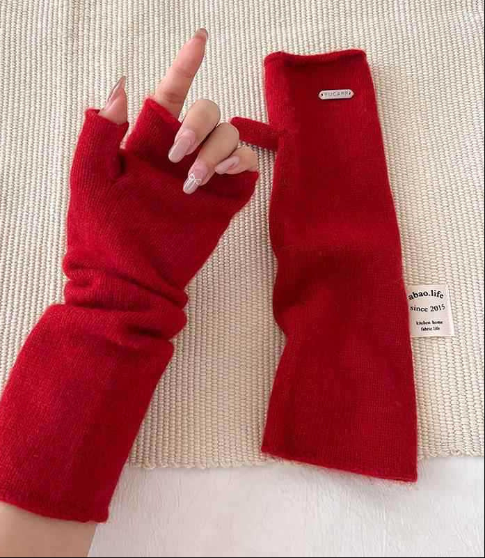 Red fingerless knit arm warmers with thumbhole, paired gloves on textured surface