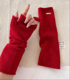 Red fingerless knit arm warmers with thumbhole, paired gloves on textured surface