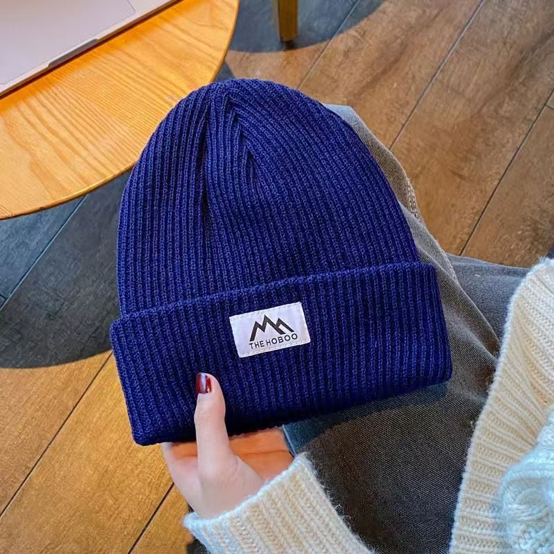 Navy ribbed knit beanie with folded cuff and woven brand patch, held by hand.