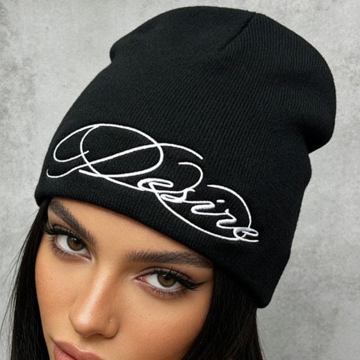 Black ribbed knit beanie with white embroidered script lettering on the cuffless fold.