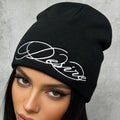 Black ribbed knit beanie with white embroidered script lettering on the cuffless fold.