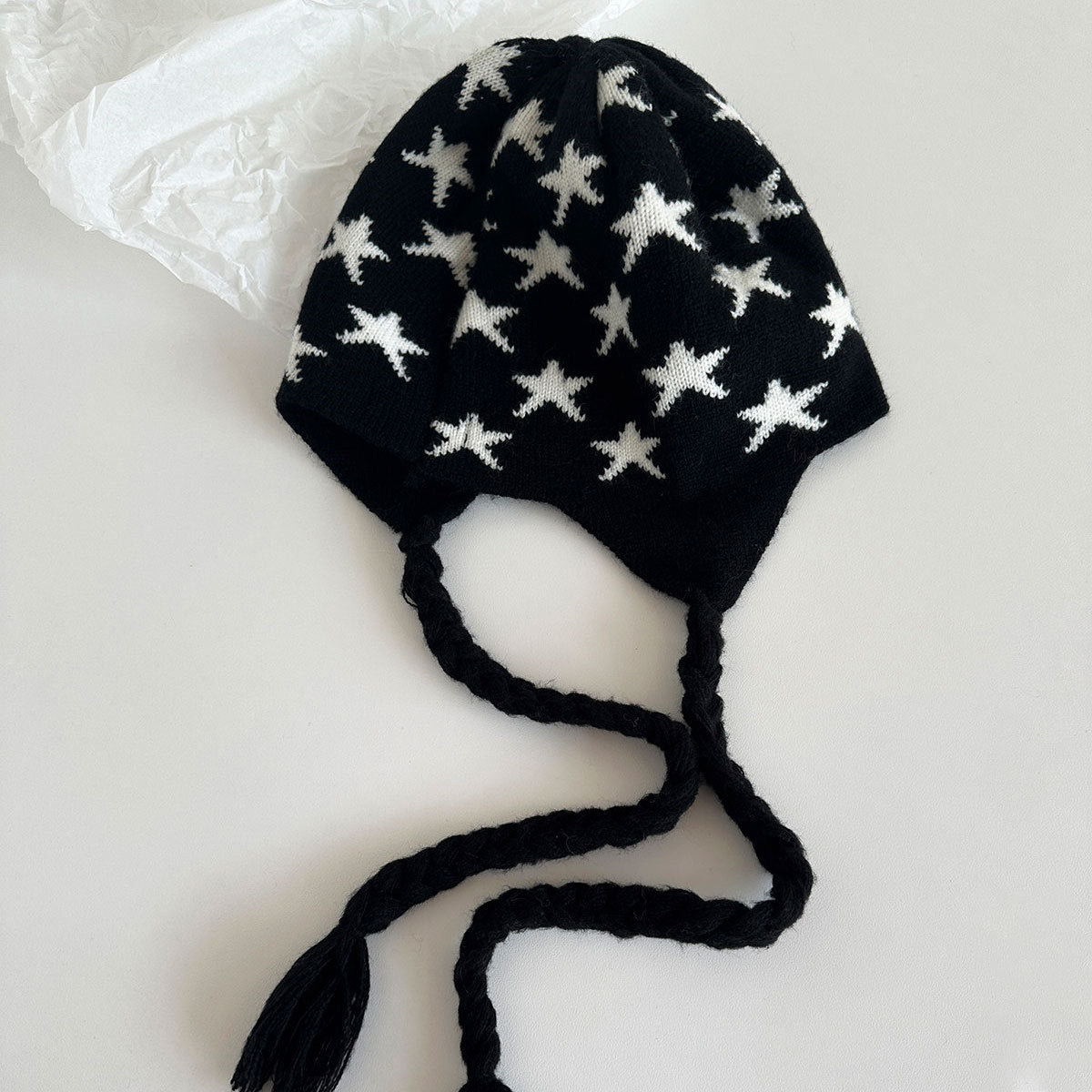 Laid-flat black knit star beanie with ear flaps and long braided tie strings.