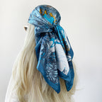 Blue satin square scarf with tropical floral print, tied as a head/neck wrap.