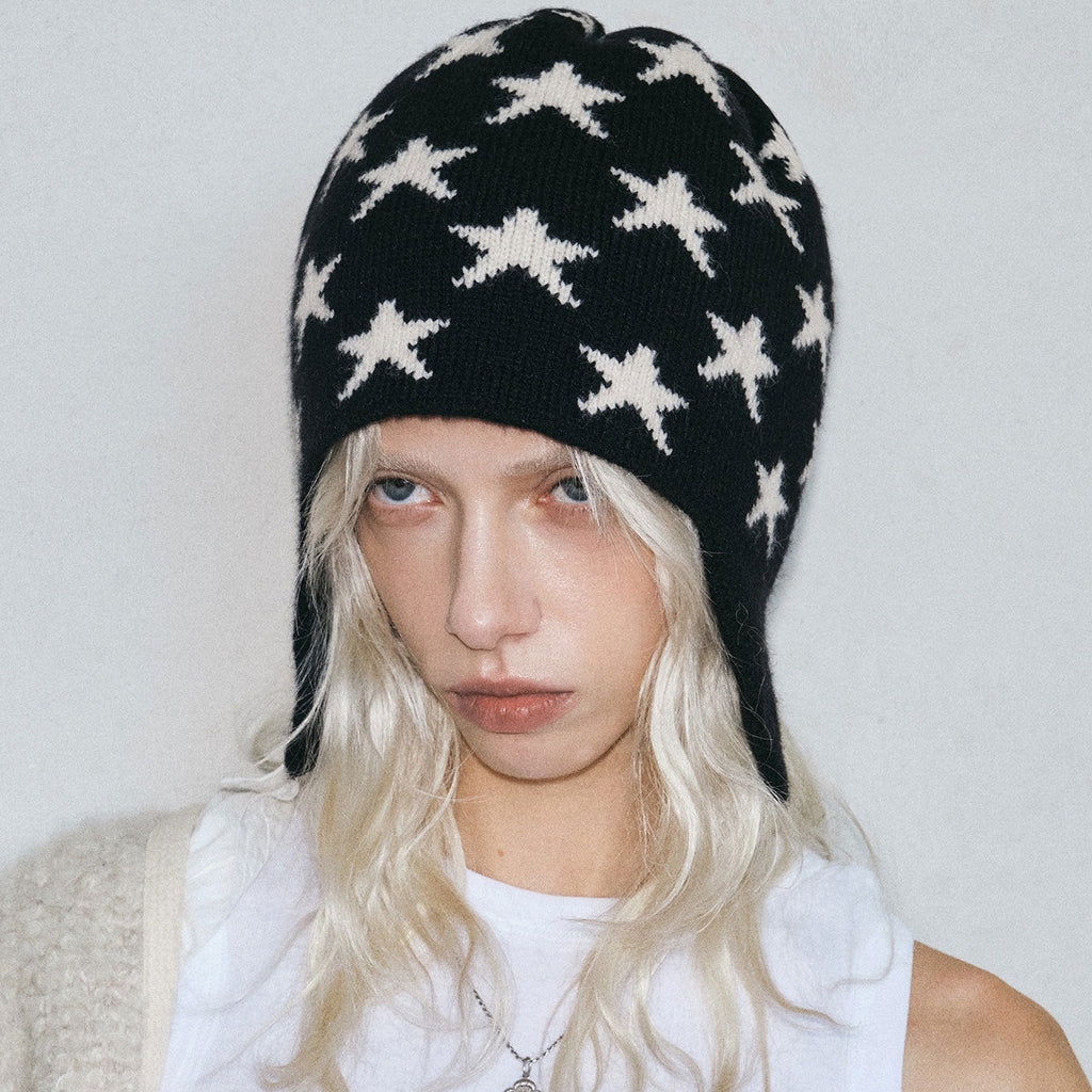 Black knit beanie with white star pattern and ear flaps, braided tie ends.