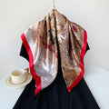 Camel satin square scarf with tropical pattern and red border, draped on black dress.