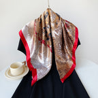 Camel satin square scarf with tropical pattern and red border, draped on black dress.