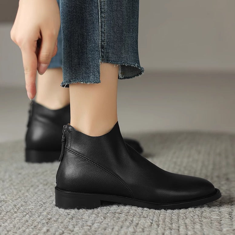 Black leather ankle boots with low block heel and back zip, foot on carpet