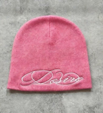 Pink knit beanie with white embroidered script lettering, flat lay front view.