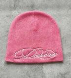 Pink knit beanie with white embroidered script lettering, flat lay front view.