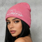 Pink ribbed knit beanie with white embroidered script lettering, cuffless slouch style.