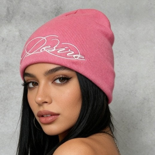 Pink ribbed knit beanie with white embroidered script lettering, cuffless slouch style.