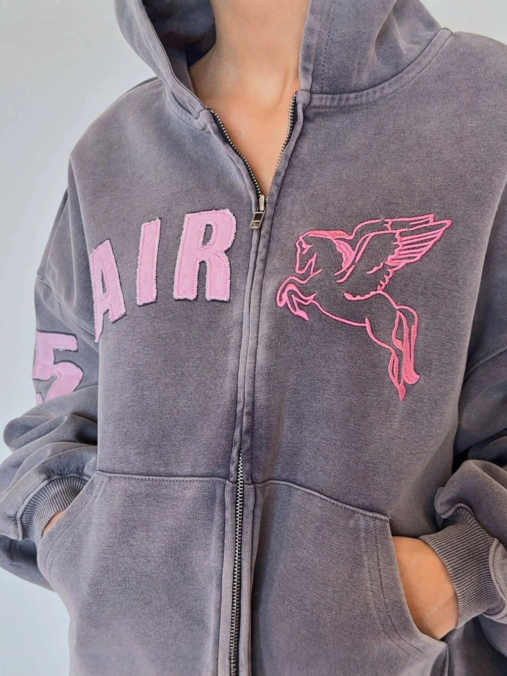 Cropped gray zip-up hoodie with hood and front zipper, pink AIR lettering and winged horse