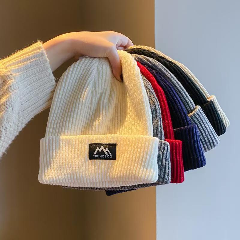 Beige ribbed knit beanie with folded cuff and woven brand patch.