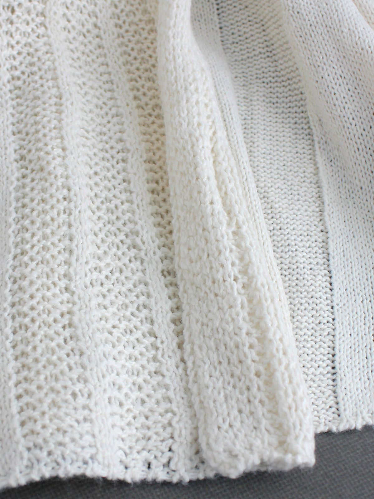 Off-white pointelle knit cardigan close-up with open-front drape panel texture