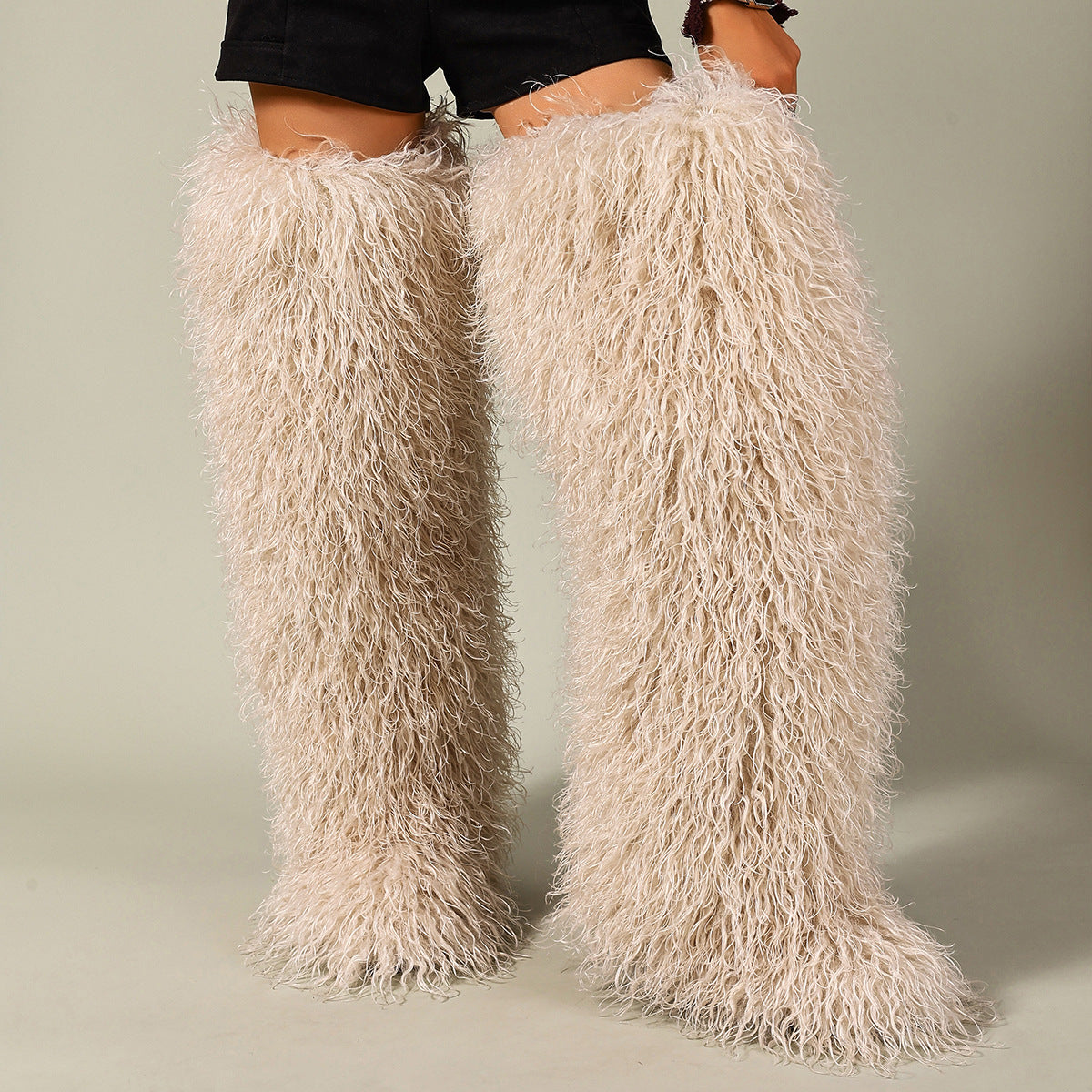 Beige faux fur thigh-high boots with long shaggy pile, worn as a pair.