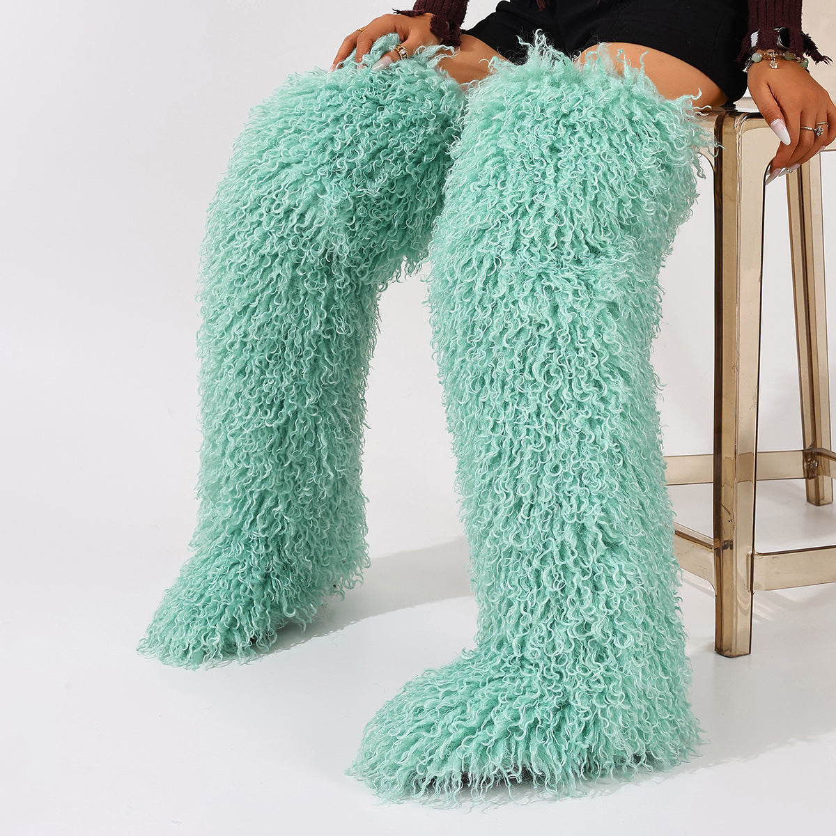 Mint green curly faux fur thigh-high boots shown worn as a pair.