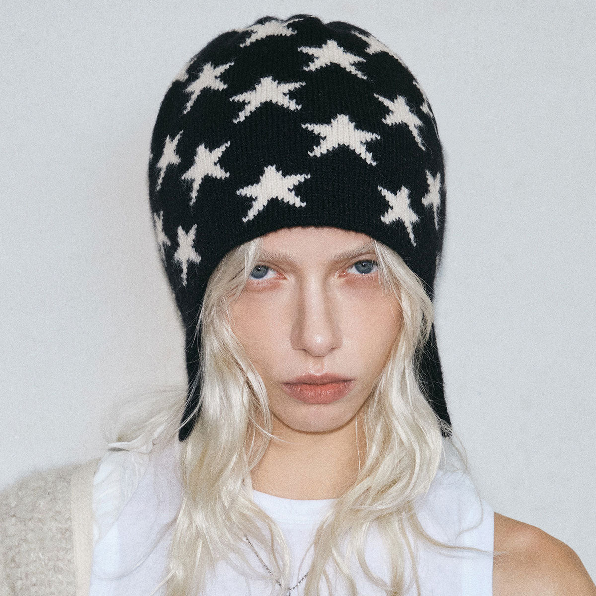 Women’s black star knit trapper beanie with ear flaps and braided tie ends.
