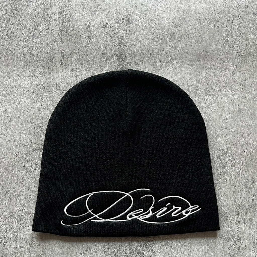 Black knit beanie with white embroidered script lettering, flat lay front view.