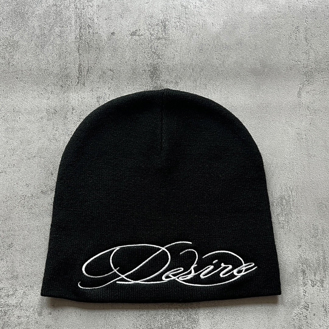 Black knit beanie with white embroidered script lettering, flat lay front view.