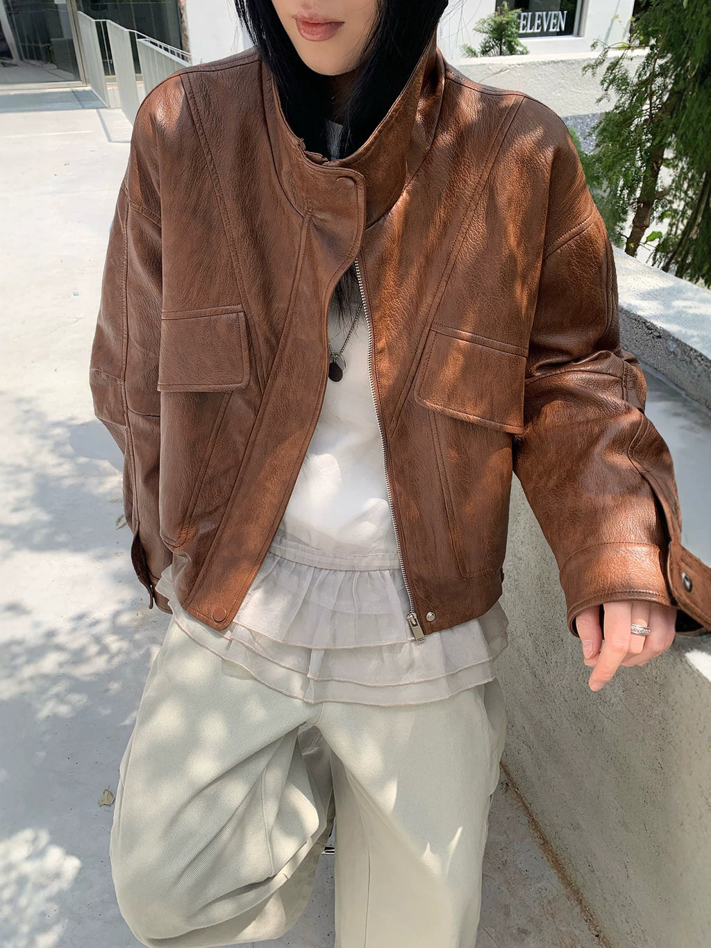 Cropped brown faux leather jacket with stand collar, zip front, and flap pockets