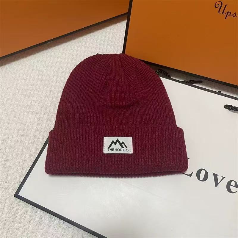 Burgundy ribbed knit beanie with folded cuff and woven brand patch.
