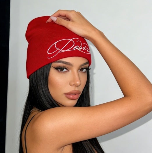 Red ribbed knit beanie with white embroidered script lettering, worn slouchy.