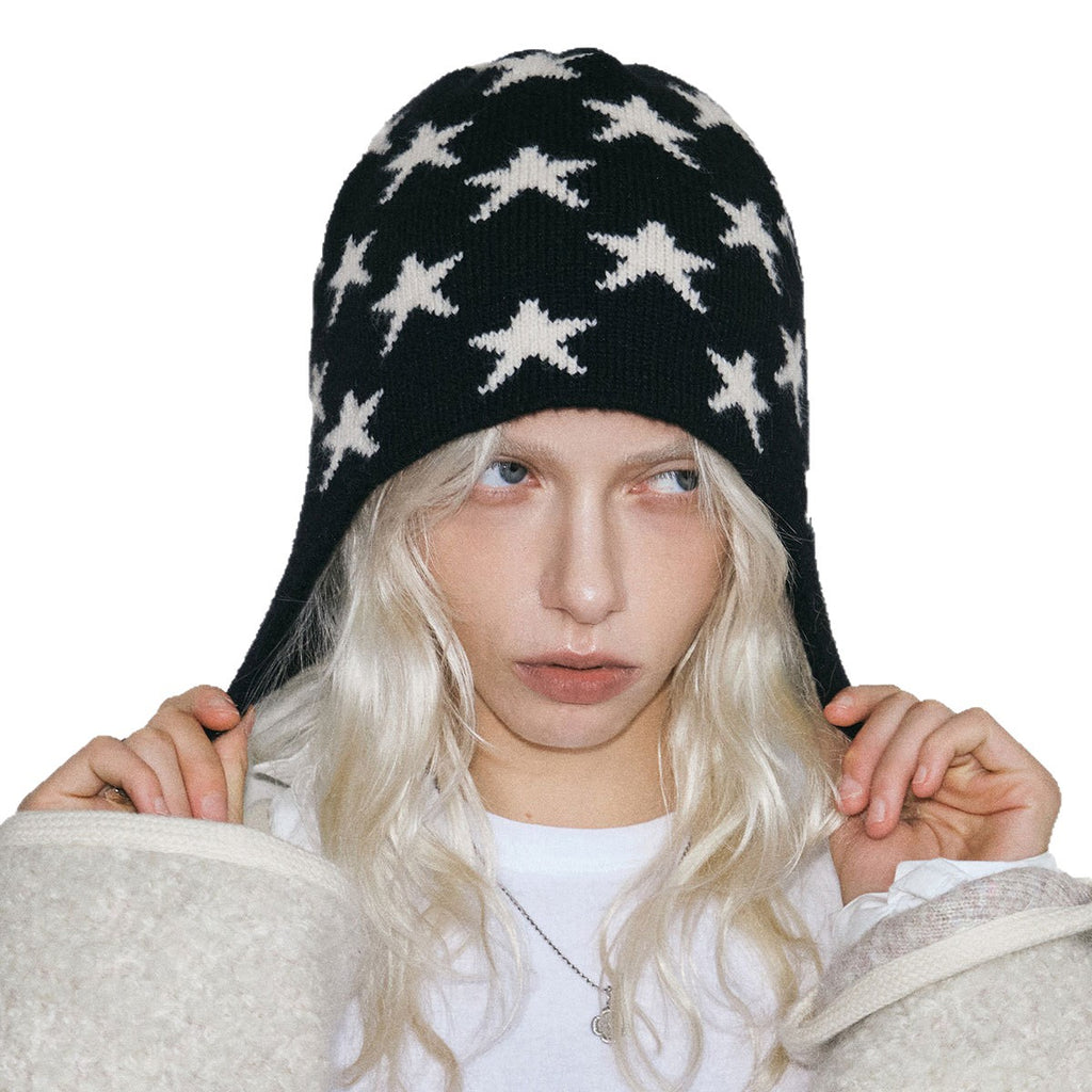 Black beanie with white star knit pattern and braided ear-flap ties, close-up.