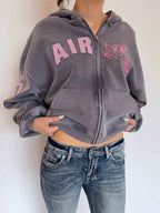 Cropped gray zip-up hoodie with hood, front zipper, pink AIR lettering and horse patch