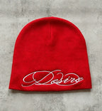 Red knit beanie with white embroidered script lettering, flat lay front view.