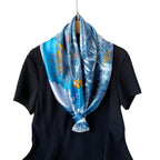 Blue satin square scarf with tropical floral print, neatly knotted at the neck.