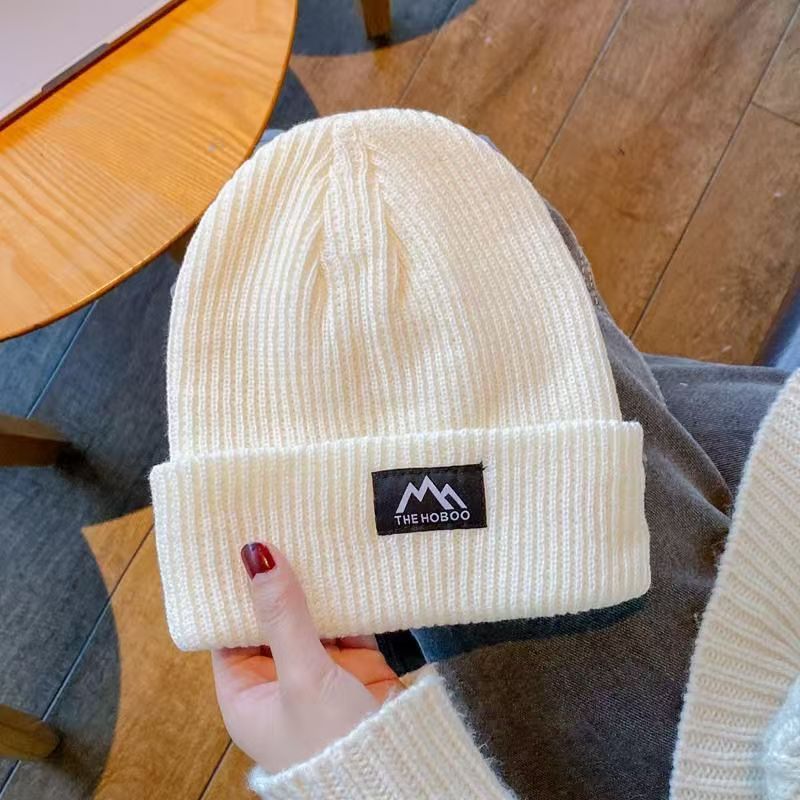White ribbed knit beanie with folded cuff and woven brand patch.