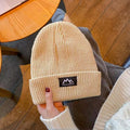 Beige ribbed knit beanie with folded cuff and woven brand patch, held by hand.