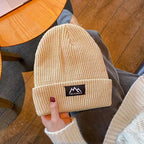 Beige ribbed knit beanie with folded cuff and woven brand patch, held by hand.