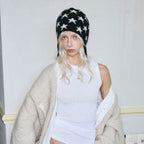 Star-patterned black knit beanie with ear flaps and braided ties, side view.