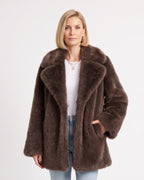 Brown fluffy faux fur coat with wide lapels and a hand tucked into a side pocket