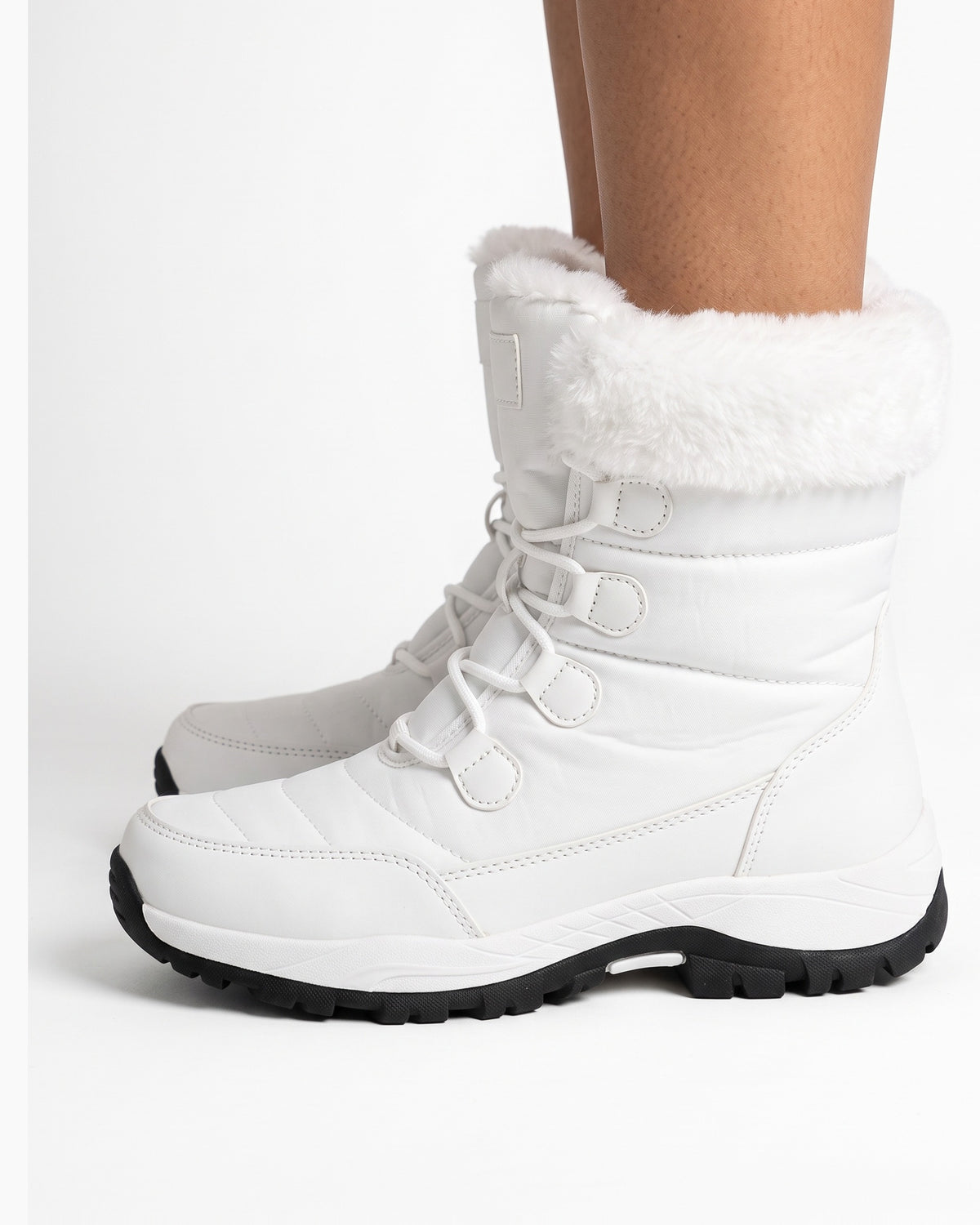 Women’s white faux fur lined lace-up snow boots on model, side view with lug sole.