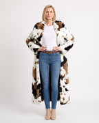 Long white faux fur coat with black and brown cow-print patches, worn open.